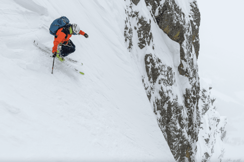 Photo of a skier descending a steep snowy cliff.